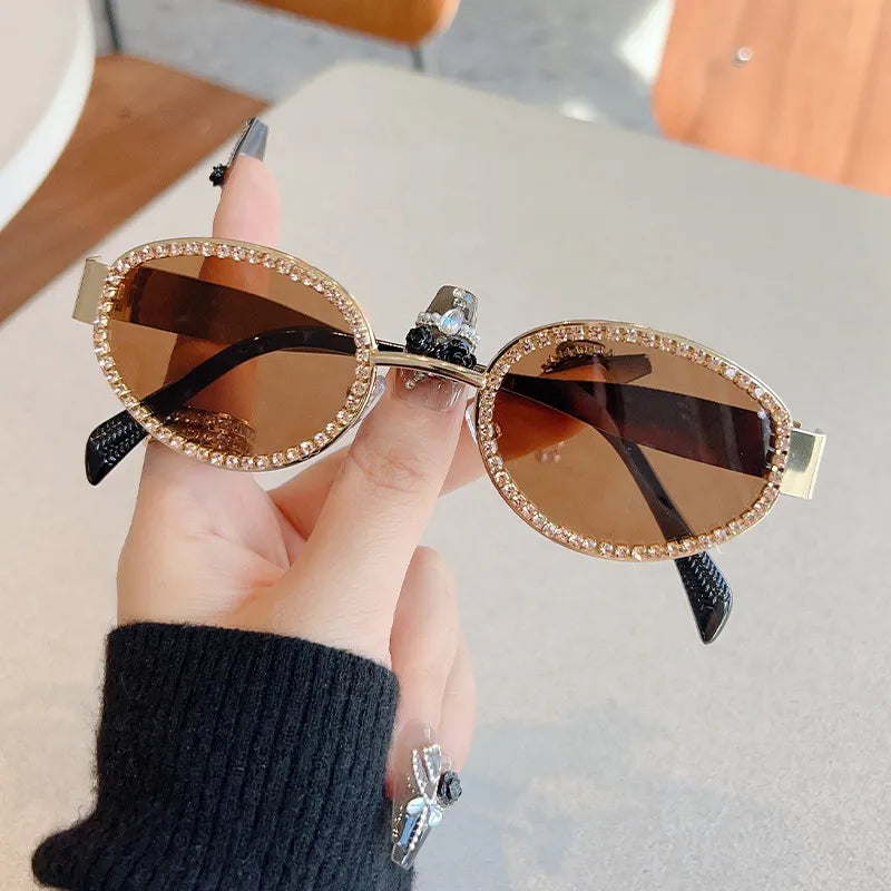 Óculos de sol ovais dourados com lentes castanhas e detalhe brilhante